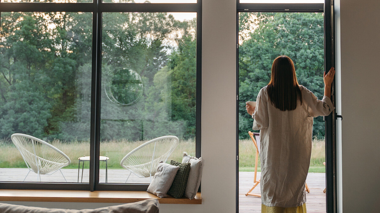 Femme de dos qui contemple la nature depuis l'intérieur de sa maison